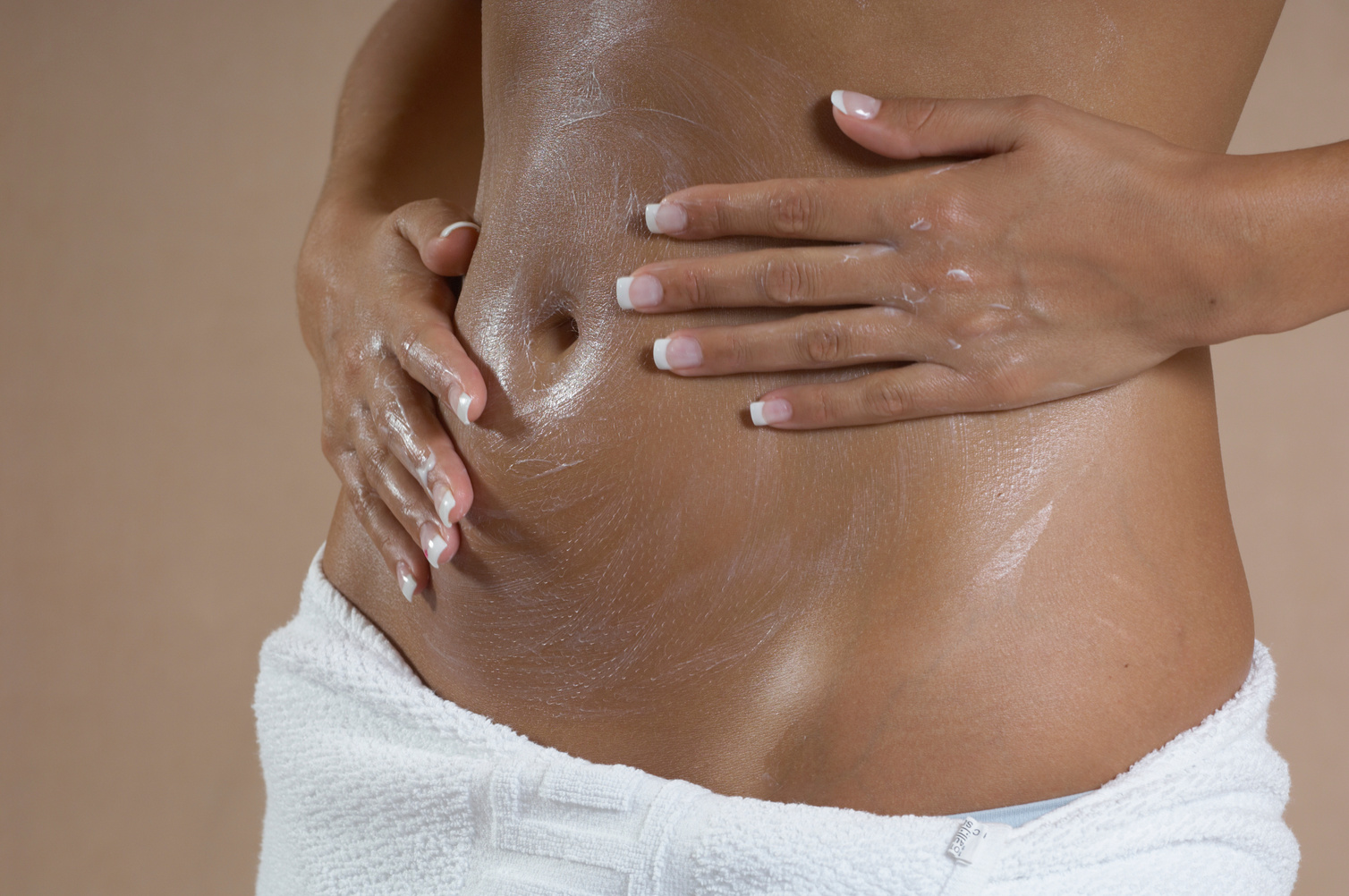 'Woman putting lotion on stomach, mid section'